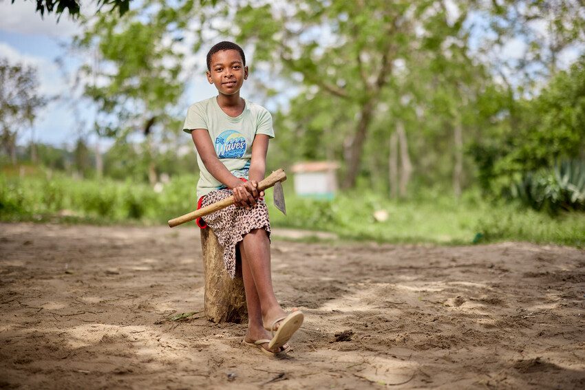 Elizabeth sits holding a farming tool. 